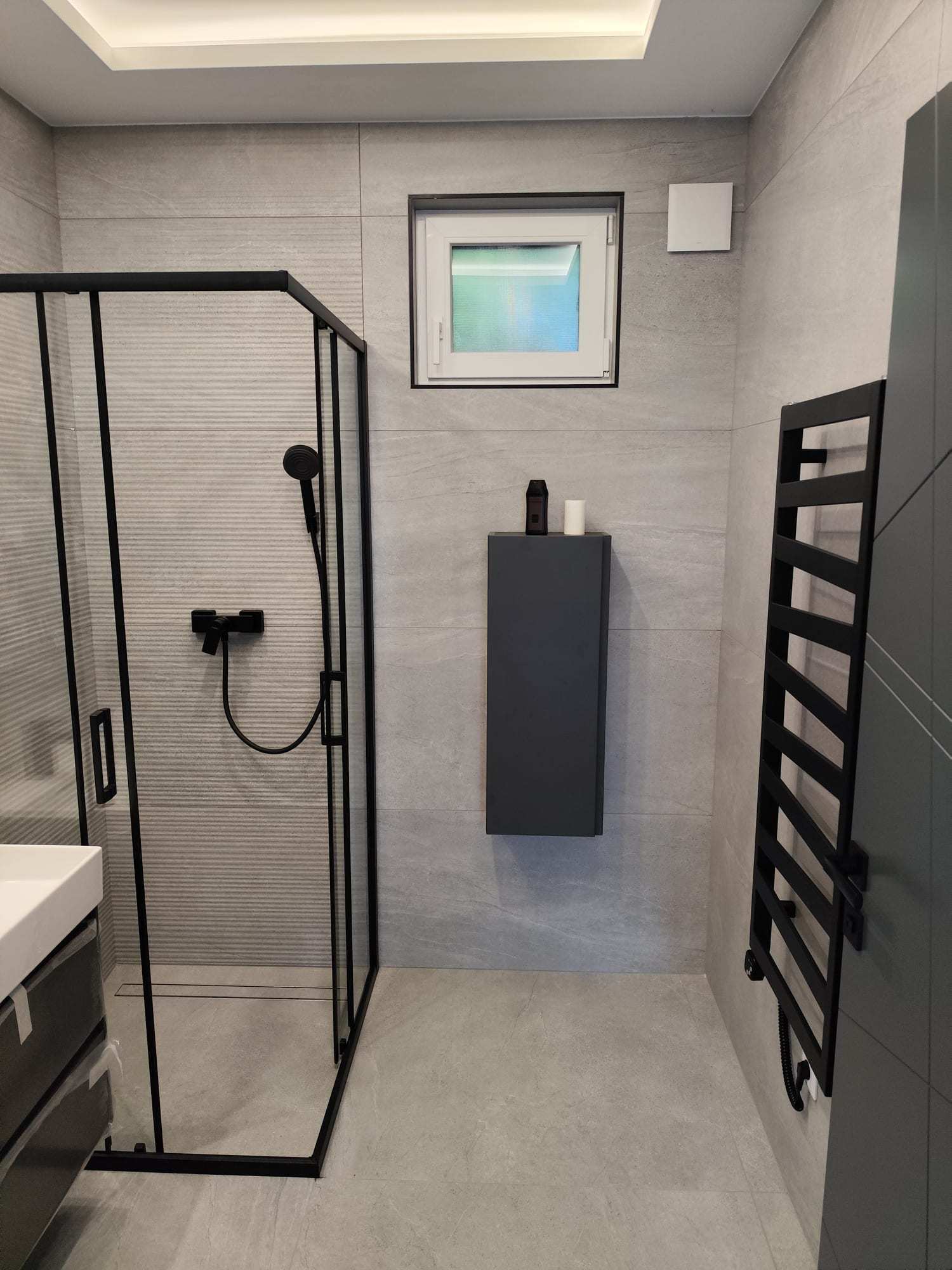 Fürdőszoba fekete zuhanykabinnal és design törölközőszárítóval